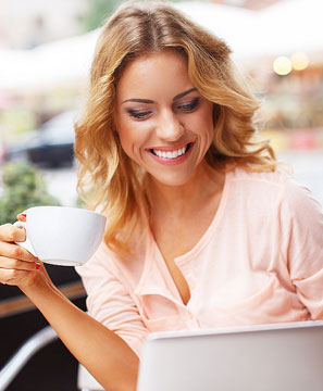 A woman smiling while drinking coffee at an outdoor cafe.